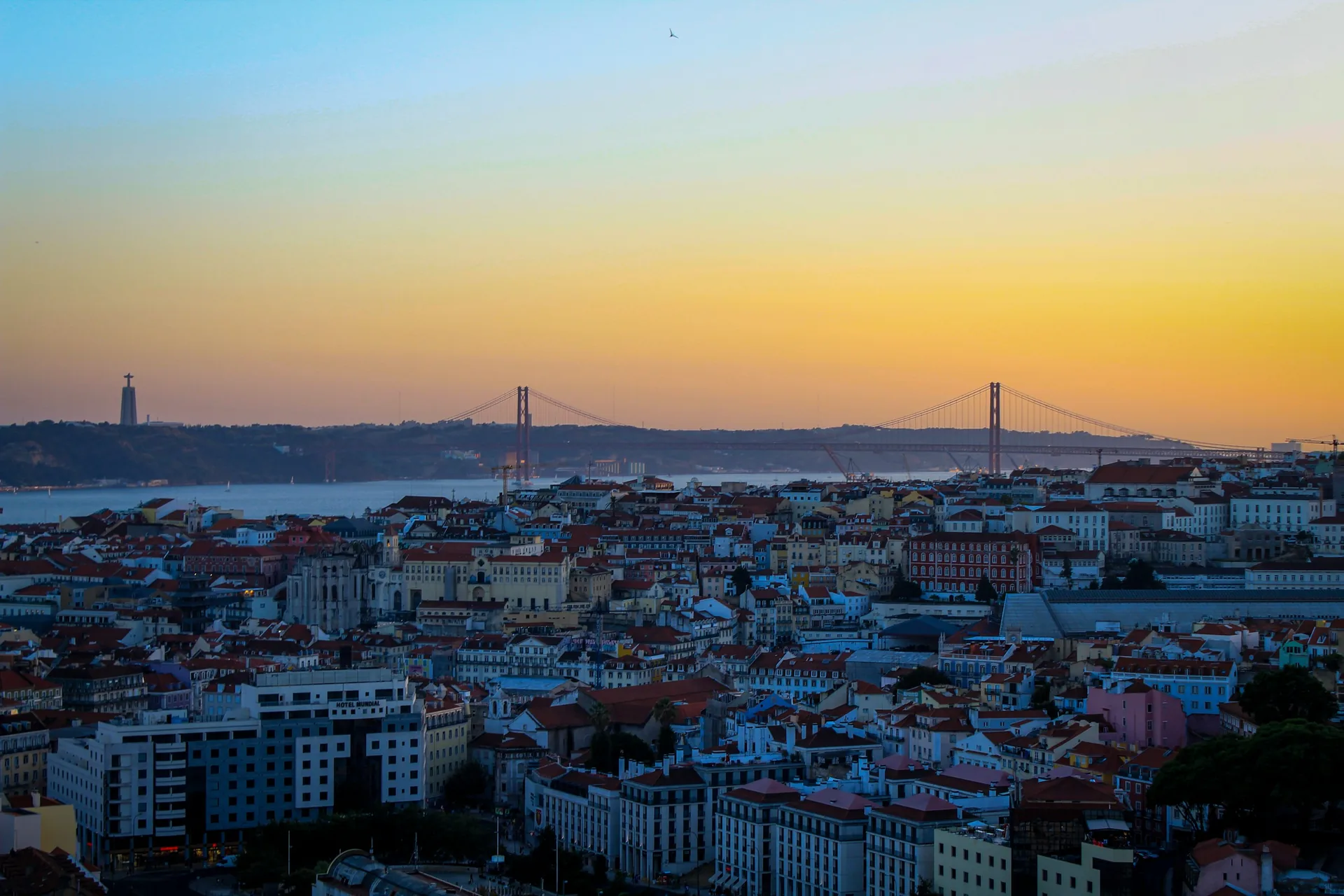 Lisbon rooftops overlooking the Tagus and the 25 de Abril Bridge at sunset